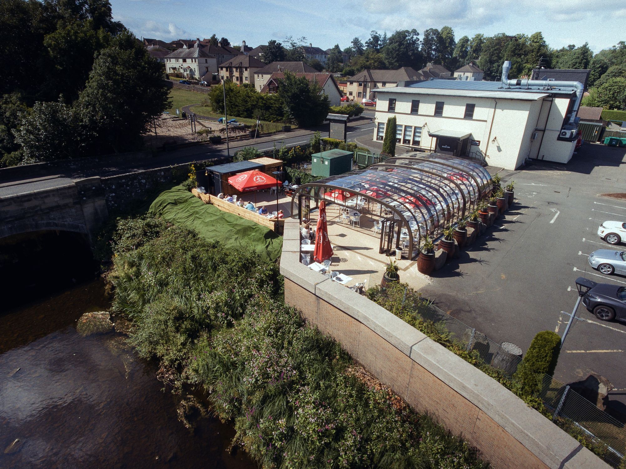Aerial view of The River Inn glasshouse beside the river and the old stone bridge