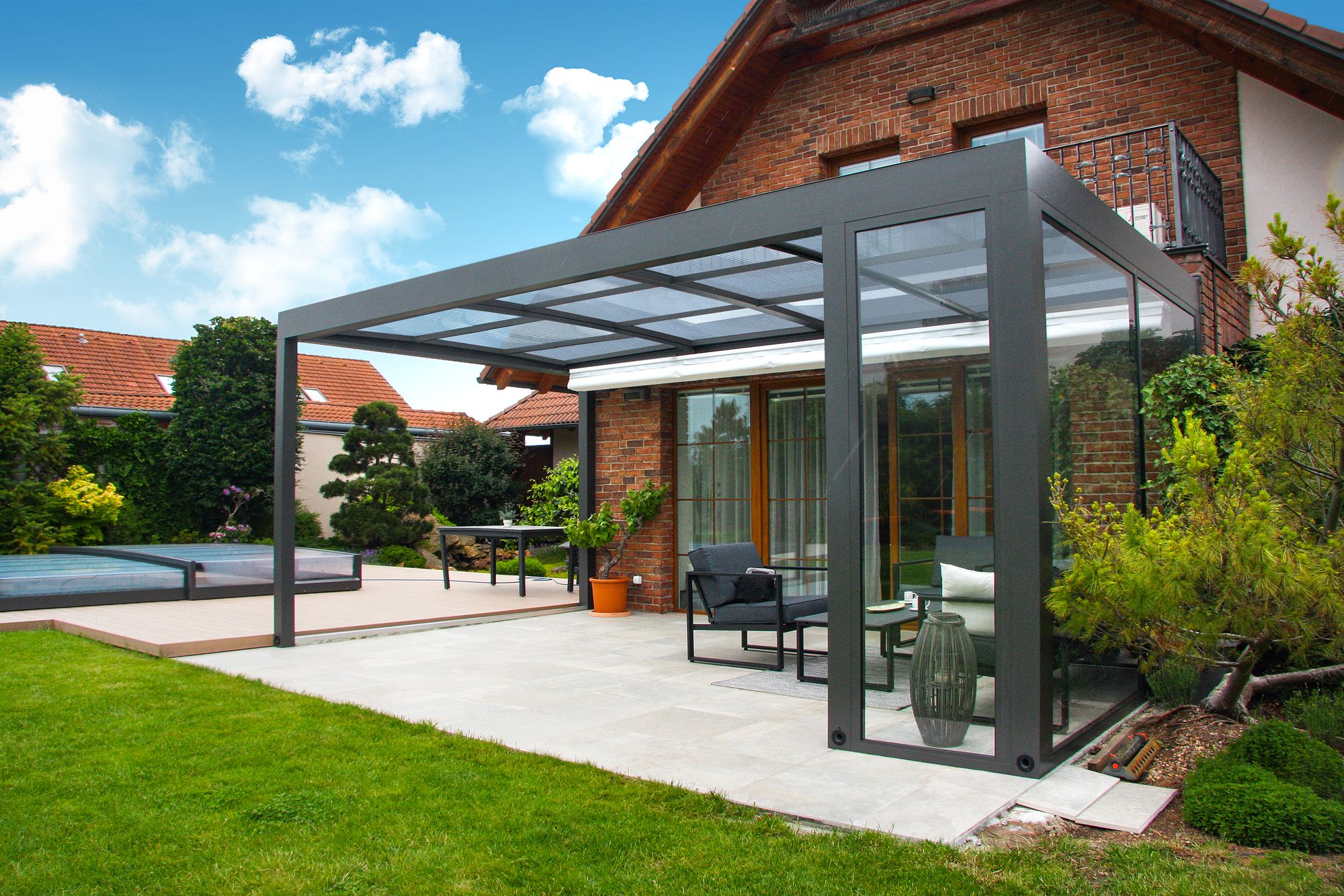 A glass room built off the back of a brick house, its roof and sliding walls in dark grey aluminium