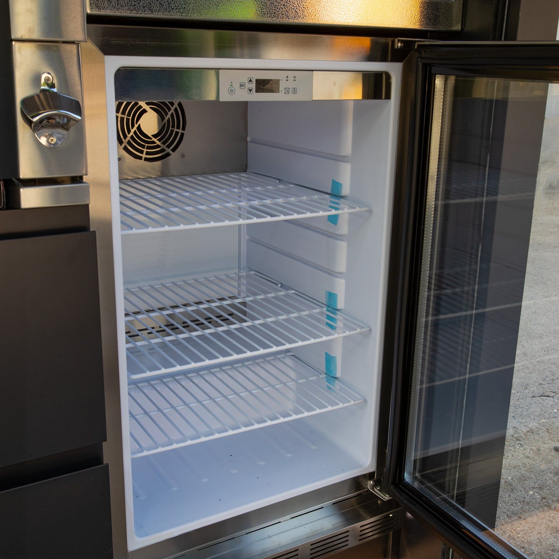 The fridge inside a cube with its door open, three wire shelves and a bottle opener beside it (supplier photograph)