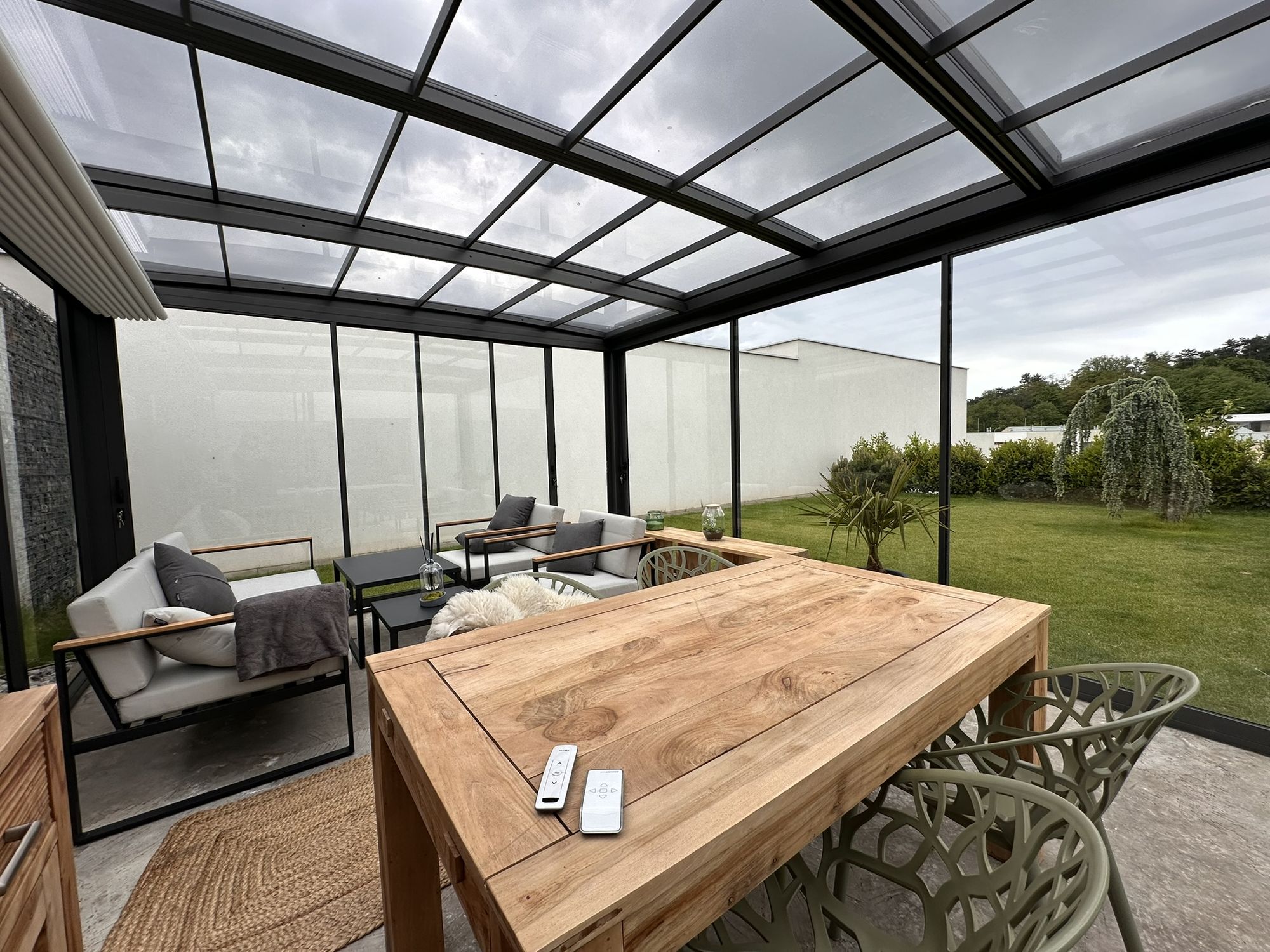 Inside a glass garden room, looking out across a dining table to the garden