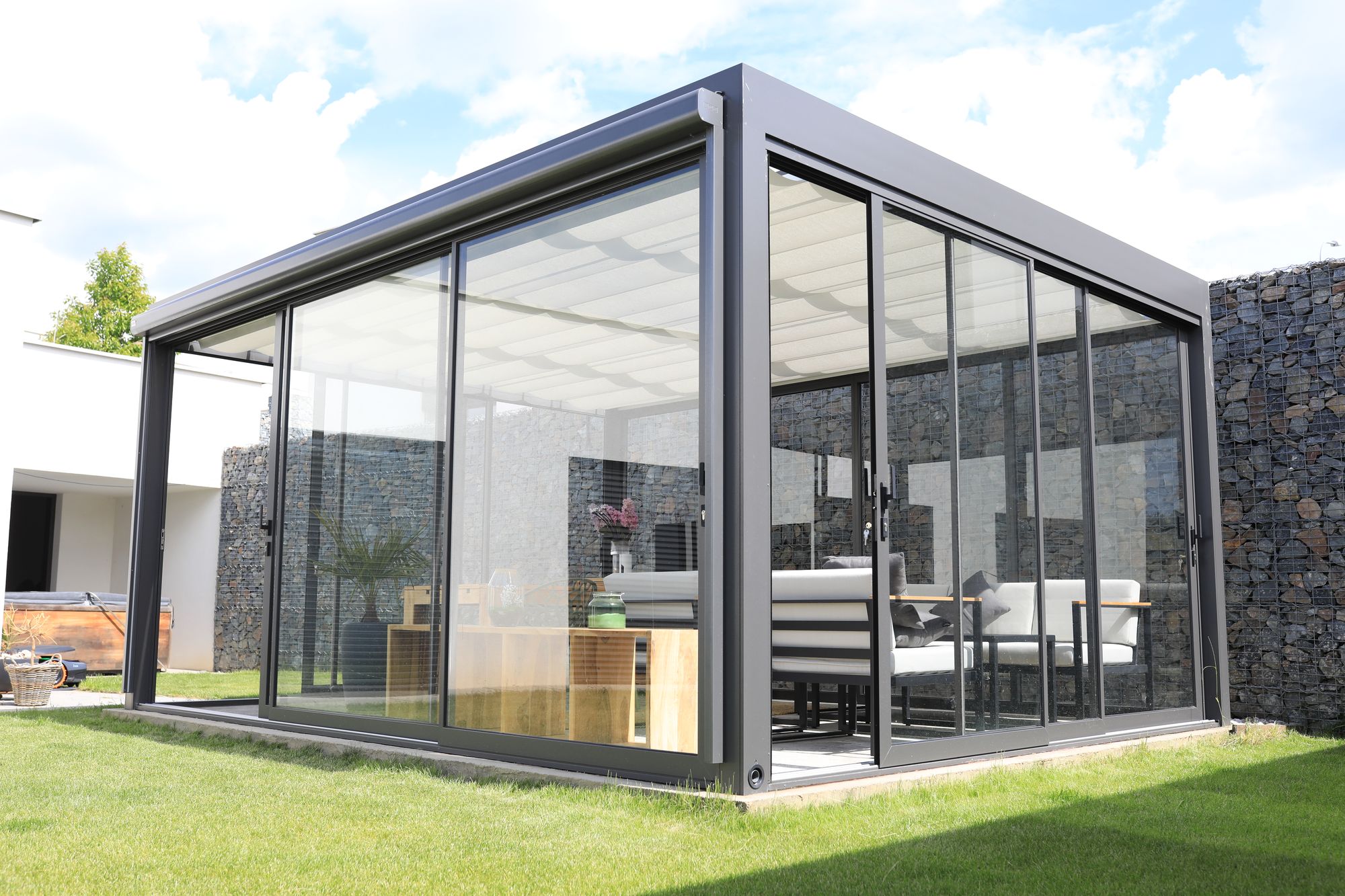 A glass garden room with its walls closed, early morning light on the lawn