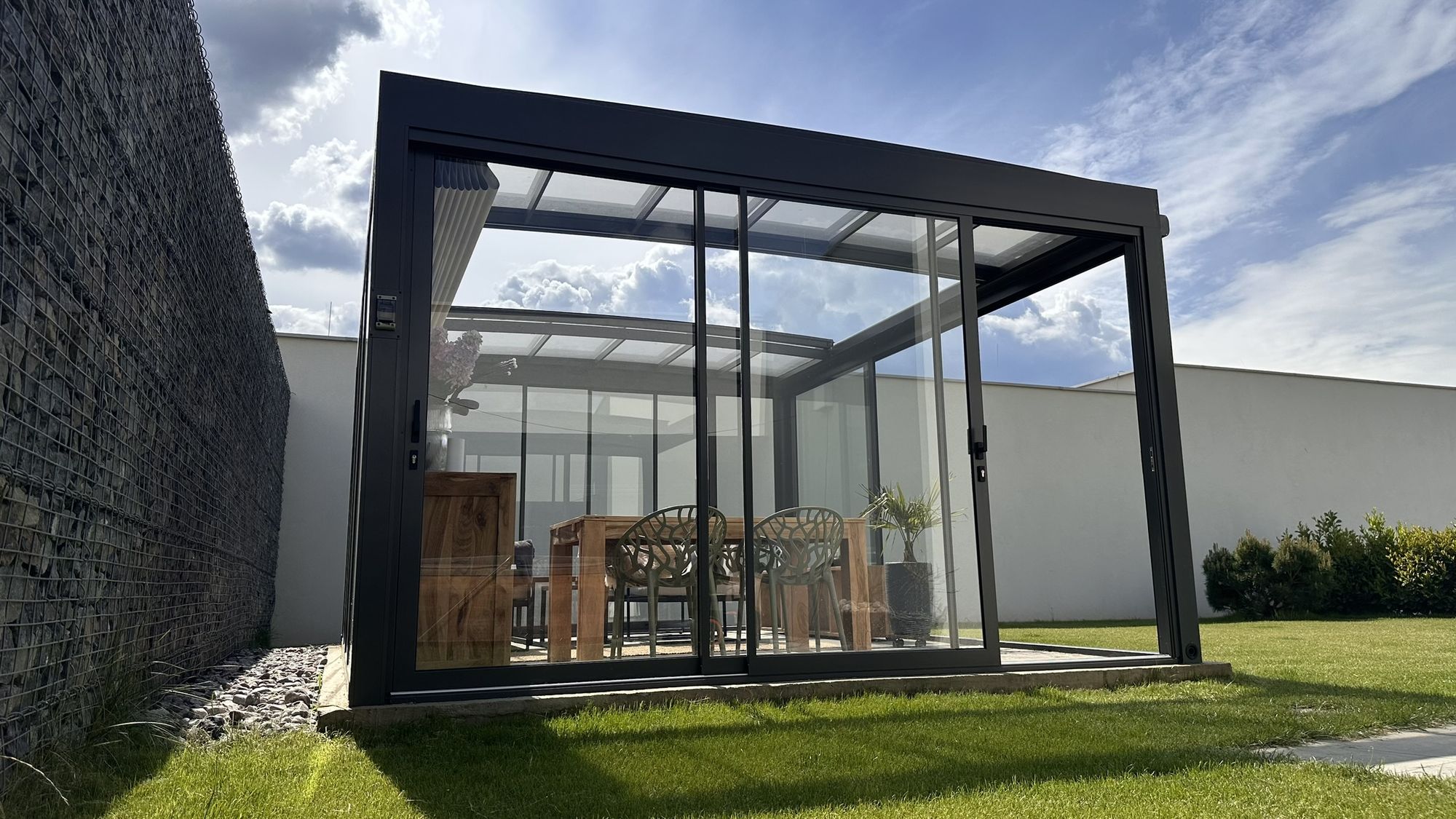 A glass room with sliding walls set against a stone boundary