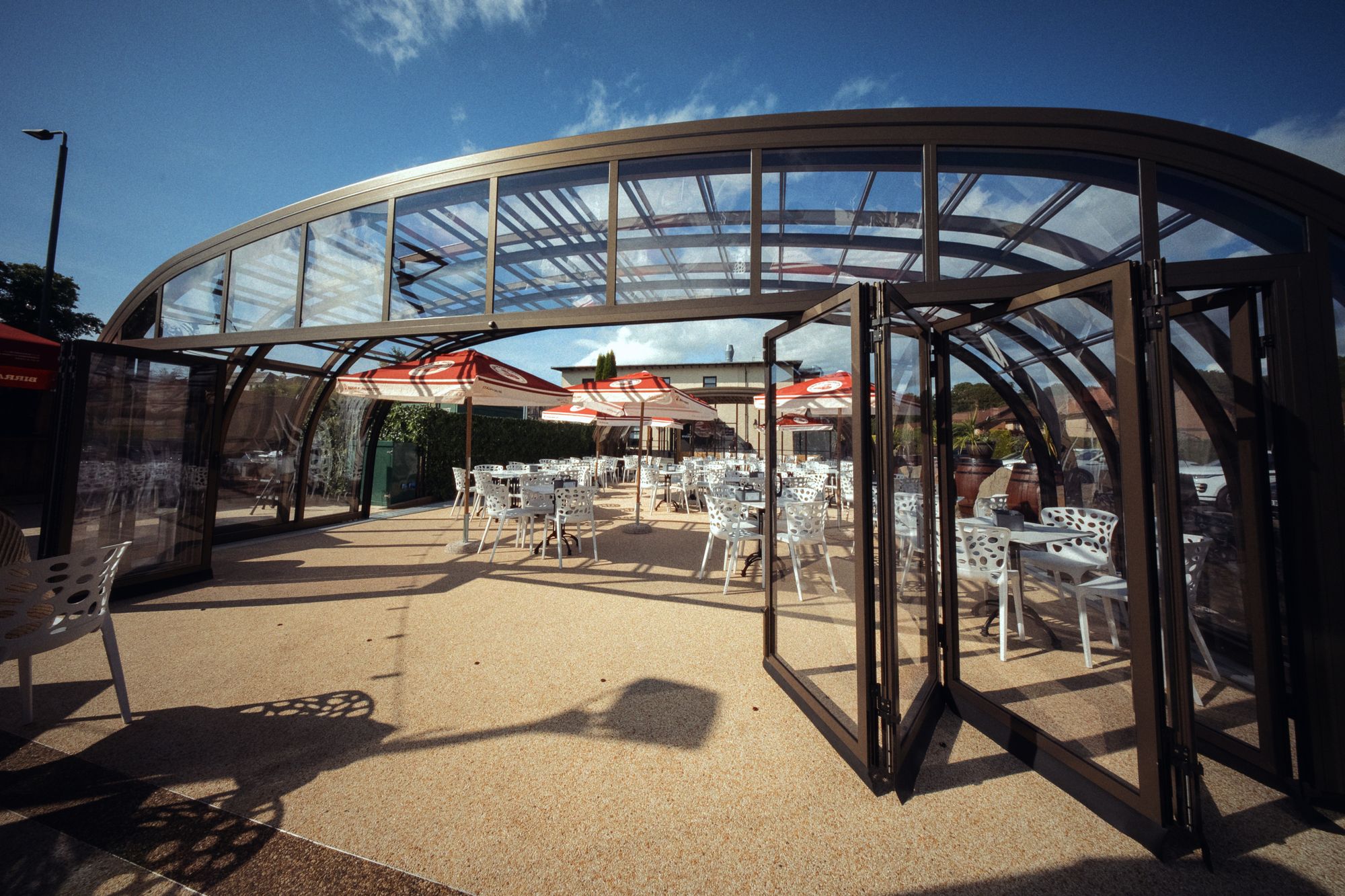 The side of the glasshouse with its folding doors pushed back, the whole flank open to the terrace